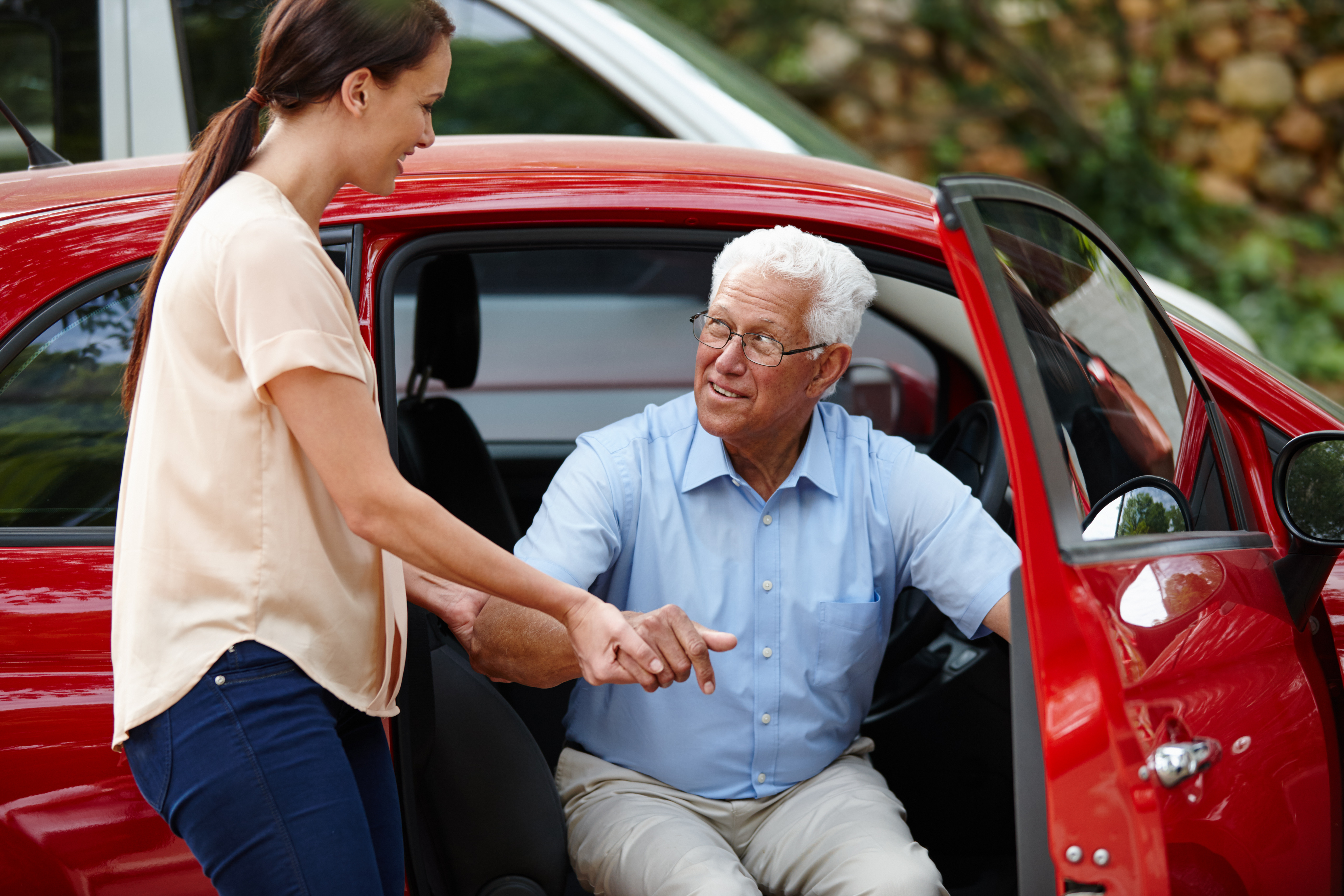 Carer helping an elderly passenger out of a Riverstone Logistics car